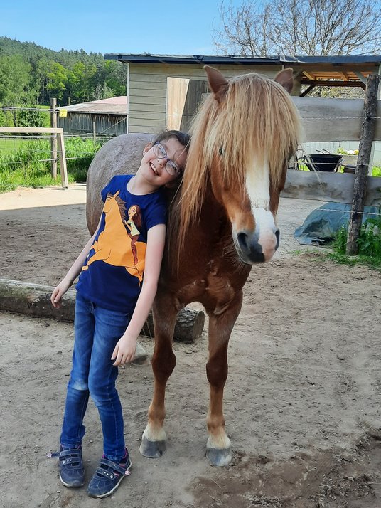 Ein Kind lehnt sich vertrauensvoll an ein ruhiges Pony