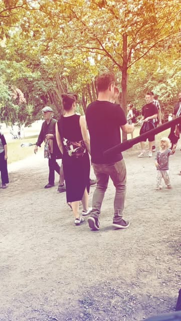 Juniper and Prayz walking together through a tree-lined festival area